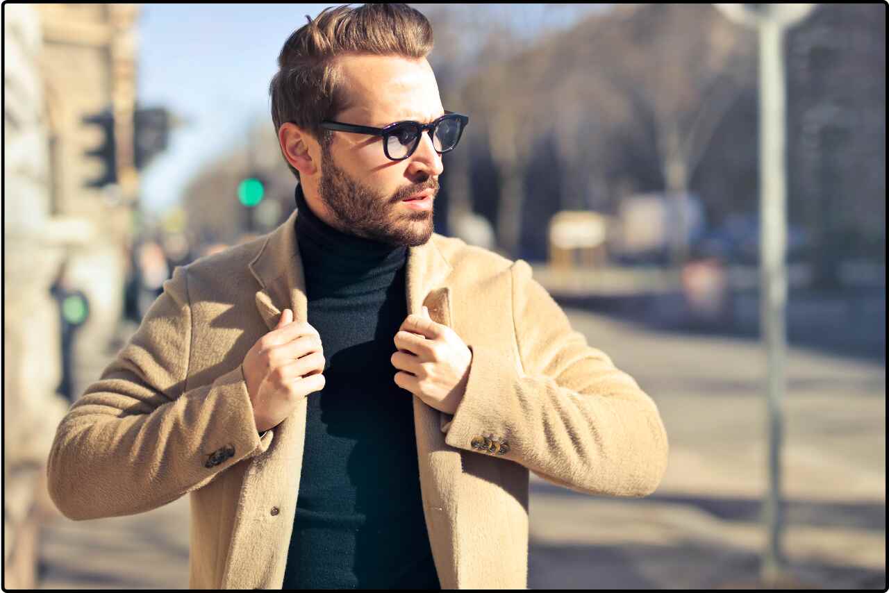 Stylish man in a brown jacket and glasses, posing confidently.